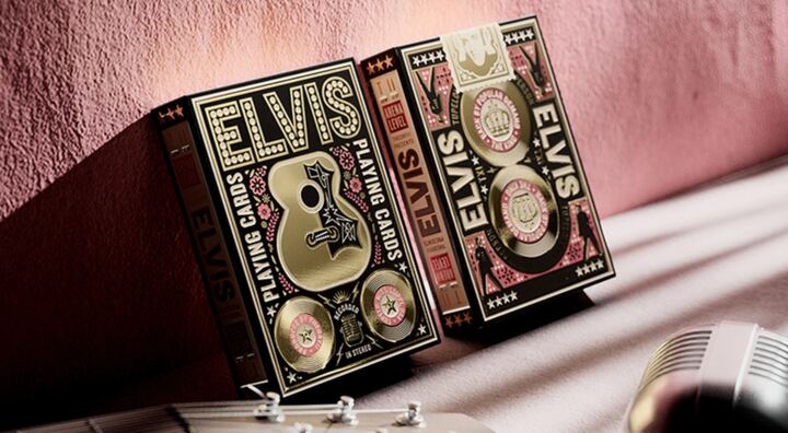 Elvis decks by theory11: black and gold boxes with a guitar motif, leaning against a pink wall.